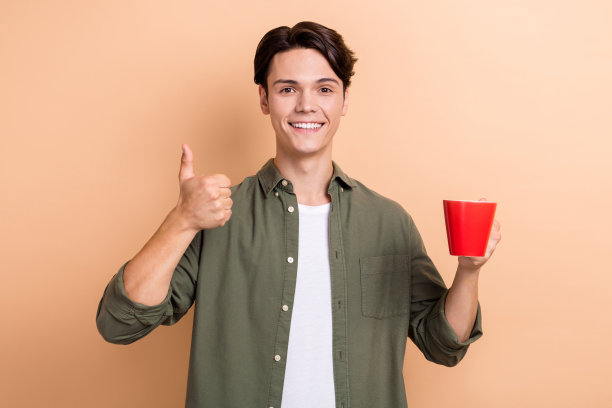 照片的牙齿喜气不错的英俊男子与深色头发穿着卡其布衬衫hold杯好工作孤立的米色背景图片下载