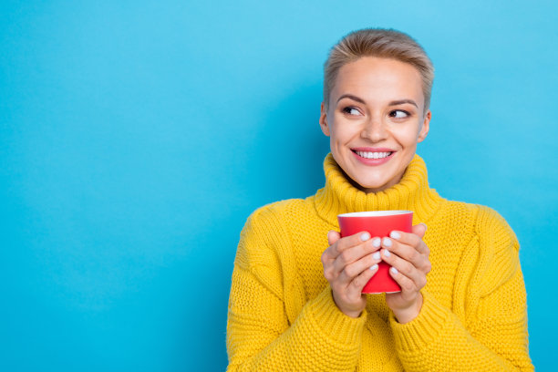 可爱体贴的女士穿着针织毛衣享受咖啡的照片，看起来空旷的空间孤立的蓝色背景图片下载