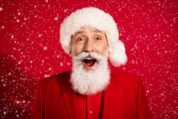 照片中，圣诞老人目瞪口呆，张大嘴巴，脸上留下深刻印象，穿着红色背景的圣诞帽图片下载