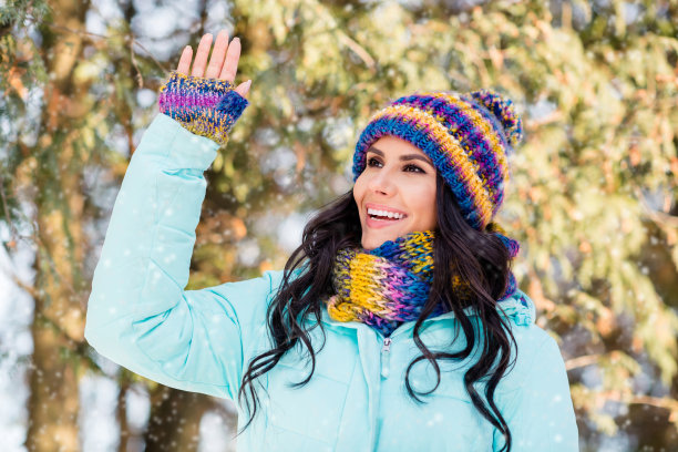 友好的女士举手问候的照片，戴针织连指手套，头饰，围巾，大衣在公园户外图片下载