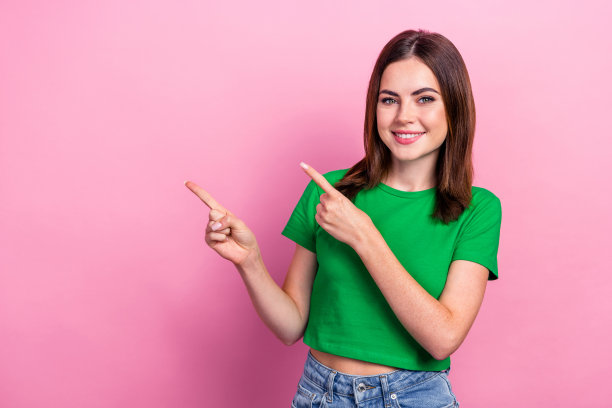 可爱可爱的开朗女孩的照片，短发，穿着绿色的t恤，在粉红色的背景上表明空白的空间图片下载