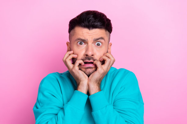 年轻有趣的鬼脸的照片害怕紧张的学生男孩咬嘴唇看恐怖电影害怕穿时髦的套头衫孤立在粉红色的背景图片下载