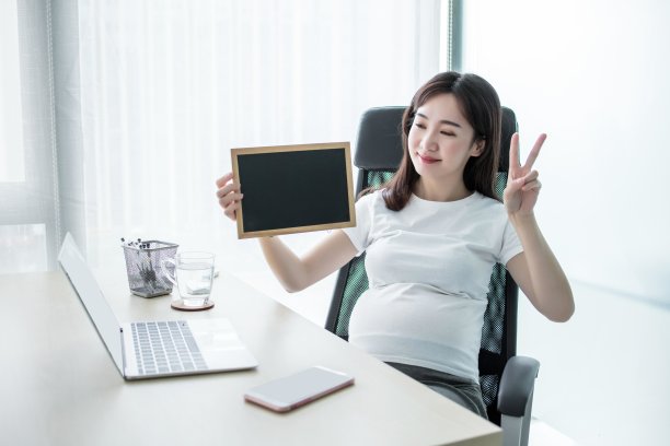 怀孕的女商人坐在办公室的办公桌前展示空白的黑板图片下载