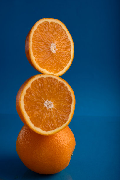 两个半橙子放在一个完整的橙子上面的照片。背景是蓝色的。橙子的切开面朝外，多汁的内部和水果的部分。图片下载