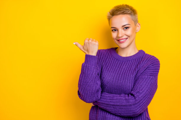 照片开朗的积极短金发促销员女人穿紫色针织毛衣拇指直接模拟提示孤立的黄色背景图片下载