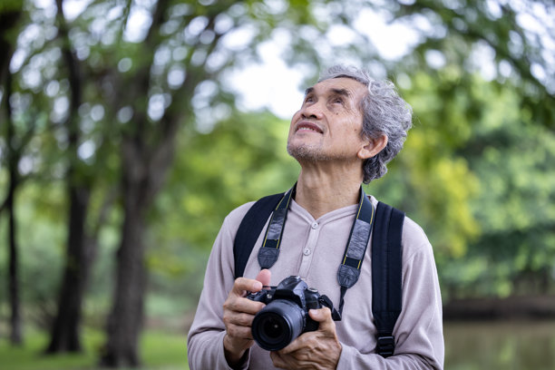 一位亚洲老人在森林里徒步旅行，用相机为老年人户外锻炼和自然环境治疗拍摄难忘的照片图片下载