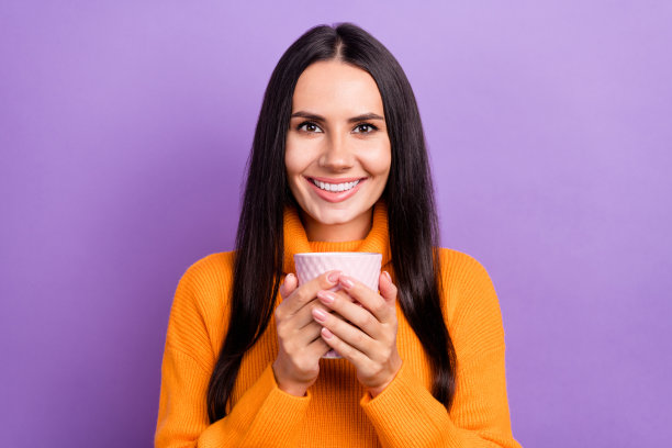 照片肖像可爱开朗满意的漂亮女人穿着橙色毛衣拿着杯热芳香咖啡孤立在紫色的背景图片下载