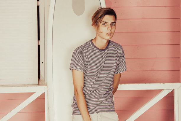 在海上度假。年轻帅气的小伙子在沙滩上拿着冲浪板。图片下载