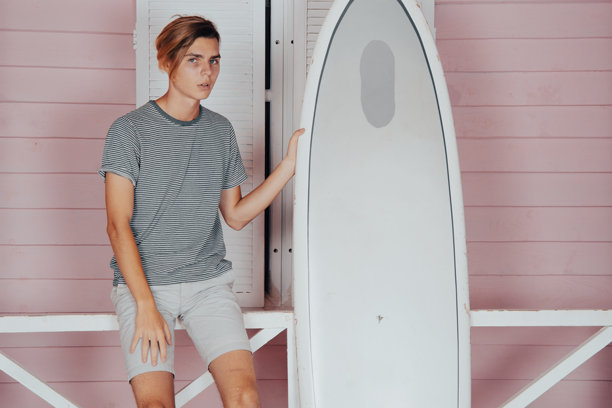 在海上度假。年轻帅气的小伙子在沙滩上拿着冲浪板。图片下载