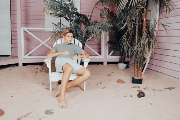 在海上度假。年轻帅气的小伙子在沙滩上拿着冲浪板。图片下载