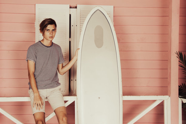 在海上度假。年轻帅气的小伙子在沙滩上拿着冲浪板。图片下载