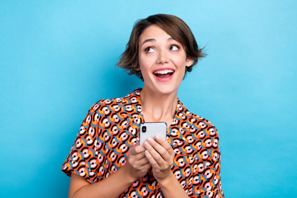 惊喜开朗的美女拿着电话的照片在蓝色的背景上看起来空无一物图片下载