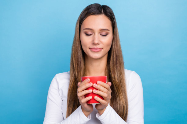 照片的梦幻迷人的女人穿着白色衬衫享受美味的温暖的咖啡孤立的蓝色背景图片下载