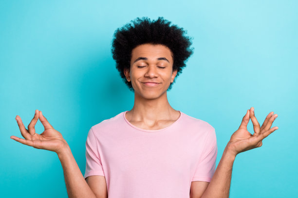 肖像照片闭上眼睛放松的学生男生chevelure发型穿粉红色时髦的t恤冥想手指瑜伽孤立在蓝色的背景图片下载