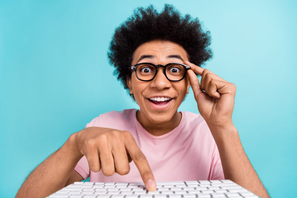 照片的年轻人粉红色的t恤点手指电脑键盘触摸眼镜惊讶意外赌博孤立在蓝绿色的背景图片下载