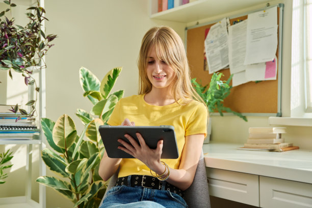 年轻的女青少年拿着数码平板电脑，坐在家里图片下载