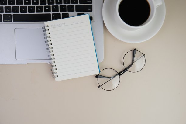 一张灰色的桌子上放着一杯咖啡、一台笔记本电脑和一本笔记本。教育、商务及办公理念。图片下载