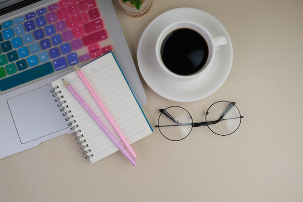 一张灰色的桌子上放着一杯咖啡、一台笔记本电脑和一本笔记本。教育、商务及办公理念。图片下载