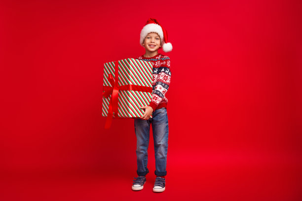 迷人的小男孩拿着大礼物庆祝圣诞节穿着针织毛衣孤立的红色背景的全身照片图片下载