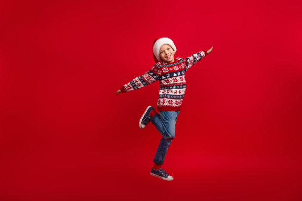 可爱的小男孩的全尺寸照片跳跃飞行摊开双手庆祝新年穿着针织服装孤立的红色背景图片下载