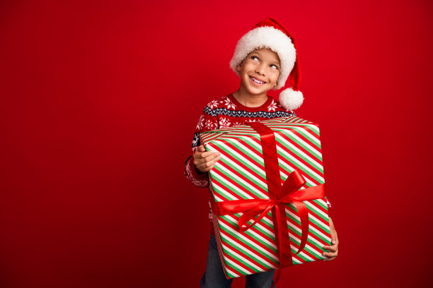 可爱小男孩的照片肖像看起来空空荡荡，拿着大礼物庆祝新年，穿着针织服装孤立在红色背景上图片下载