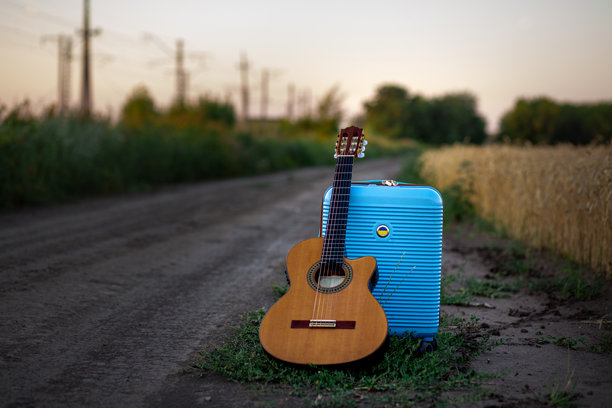 一个吉他和一个大的塑料蓝色手提箱，一个黄蓝色的旗帜，站在晚上的麦田旁边的土路图片下载