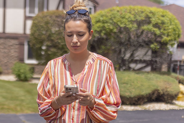 一位身穿彩色衬衫的美女站在街上玩手机的正面照片图片下载