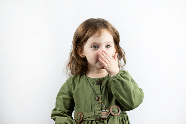 一个穿裙子的红发小女孩正在挠鼻子。一个有趣的小孩在白色背景上的工作室照片图片下载