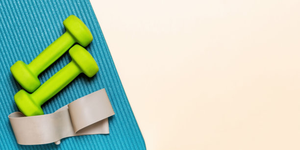 把绿色哑铃和阻力带平放在蓝色瑜伽垫上图片下载