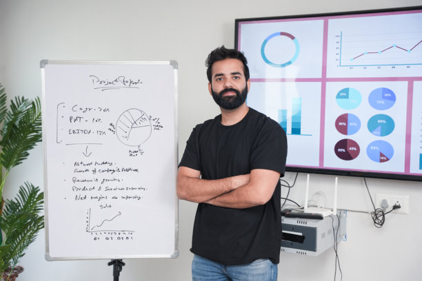 专业的印度企业家交叉手臂站在白板前的图表和图表的公司在现代办公室。销售和增长，收入和利润，战略建设。图片下载