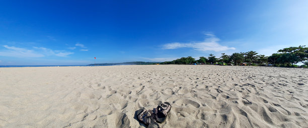 凉鞋在白色沙滩上，在阳光明媚的日子里，清澈的蓝天和远处的小山。暑假和热带海滩的概念。全景风景照片图片下载