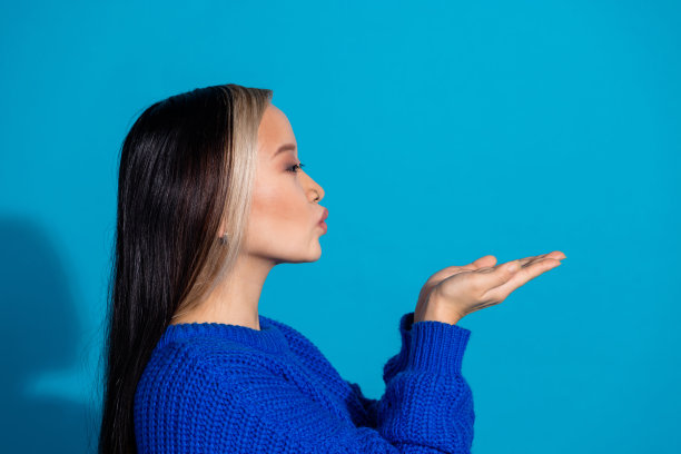 照片中迷人的年轻女子的肖像侧面送空吻空穿针织衫衣服孤立在蓝色的背景图片下载