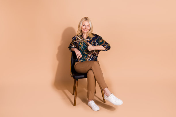 照片肖像的金发成熟年龄的女商人坐在舒适的椅子像这样的家具孤立在米色背景图片下载