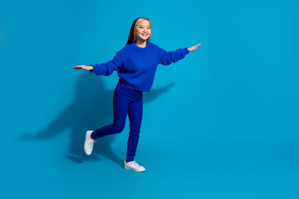 全身照片有趣的年轻时髦的女孩站在一条腿保持平衡飞行的鸟孤立在蓝色的背景图片下载