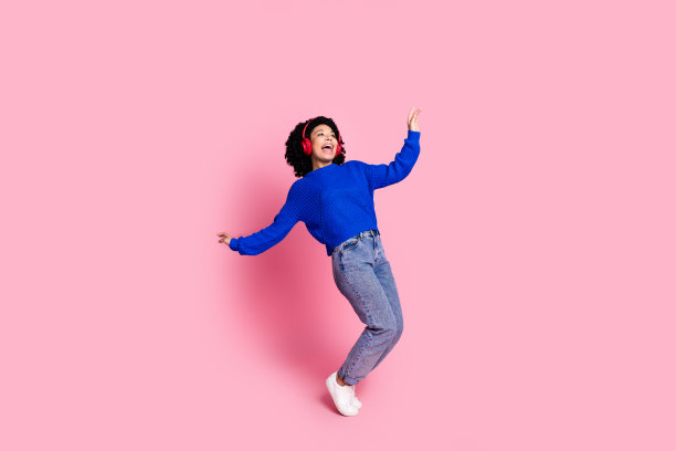 照片肖像卷曲的黑发年轻女子享受最喜欢的歌曲红色蓝牙耳机孤立的粉红色背景图片下载