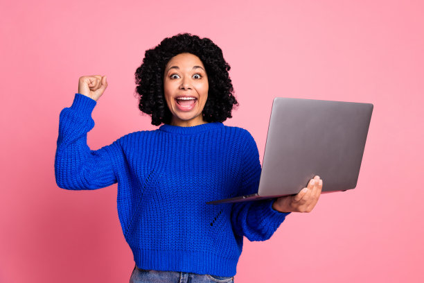 黑色波浪发女士穿着蓝色毛衣的照片使用笔记本电脑庆祝赢得伟大的周末销售孤立的粉红色背景图片下载