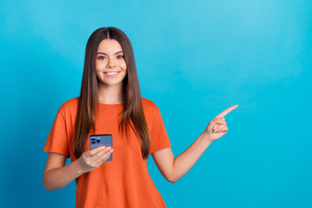 可爱的少女的照片肖像手持电话点空空间穿着时尚的橙色服装孤立在蓝色的背景图片下载