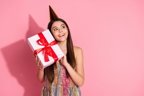 照片的快乐漂亮的女士穿着单件生日头饰得到礼物，看起来空的空间孤立的粉红色背景图片下载