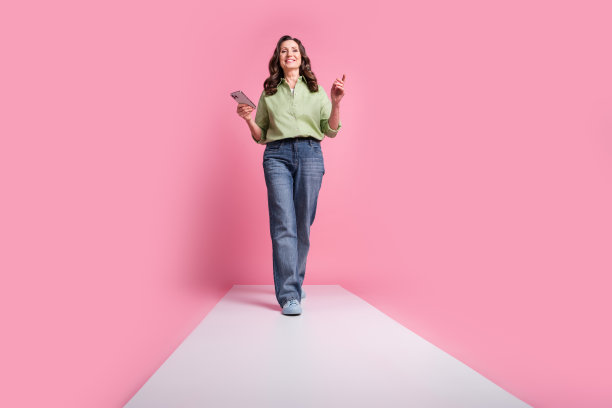 奶奶的照片，老太太穿着正装牛仔裤和卡其布衬衫，用手机走在粉红色背景的讲台上图片下载