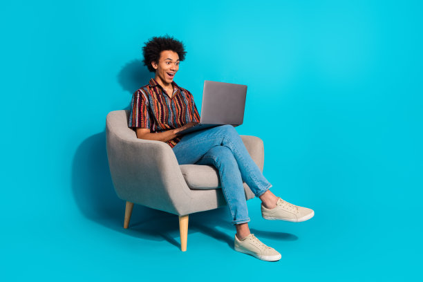 漂亮的年轻人的全尺寸照片，椅子，笔记本电脑，空的空间，穿衬衫孤立的蓝绿色背景图片下载