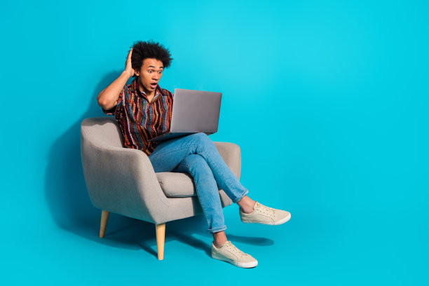 漂亮的年轻人的全尺寸照片，坐在椅子上，使用笔记本电脑，空的空间，穿衬衫孤立的蓝绿色背景图片下载