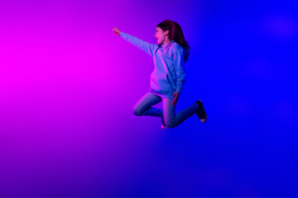 可爱可爱的小女孩穿卫衣跳高上升拳头空空间孤立品红色蓝色背景的全身照片图片下载