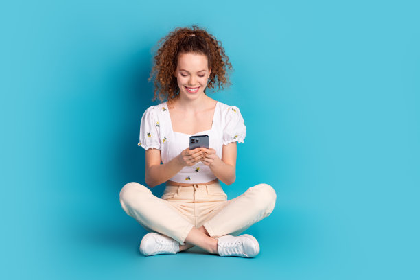 可爱的年轻女士的全身照片坐在地板小工具穿着时尚的白色服装孤立的蓝色背景图片下载