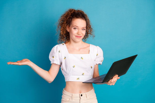 迷人的年轻女子的照片肖像拿着上网本耸肩穿着时尚的白色衣服孤立的蓝色背景图片下载