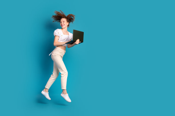 可爱的年轻女士的全身照片，转身跑步，拿着上网本，穿着时尚的白色衣服，孤立在蓝色背景上图片下载