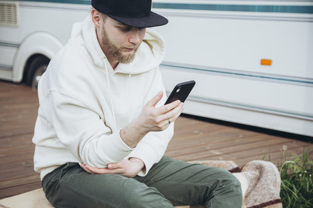 年轻的白人男子坐在汽车房外拿着电话。图片下载