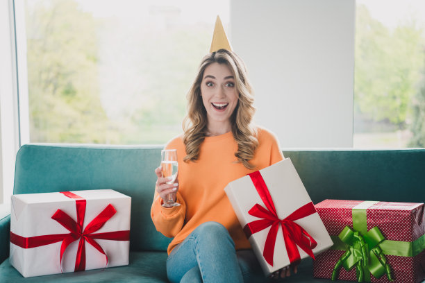 漂亮开朗的女孩的照片肖像坐在沙发庆祝生日兴奋穿着橘色的衣服度过消遣宽敞的房子室内房间图片下载