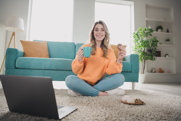 开朗的女孩全身照片坐在地板上看电影吃零食茶穿着橙色的衣服度过消遣宽敞的房子在室内房间图片下载