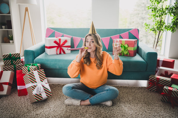 漂亮开朗的女孩全身照片坐在地板上庆祝生日兴奋地穿着橙色的衣服度过消遣宽敞的房子室内房间图片下载