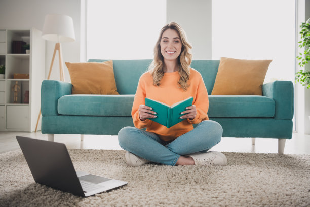 漂亮开朗的女孩全身照片坐在地板上网本看书穿着橘色的衣服度过消遣宽敞的房子室内房间图片下载